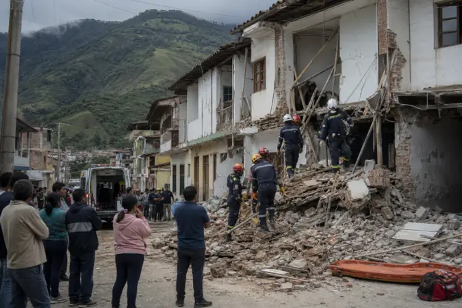 Emergency workers inspect damaged buildings on a street in western Colombia after an earthquake, with mountains in the distance.