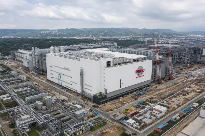 Aerial editorial illustration of a large semiconductor fabrication plant under construction in Taichung, with cleanroom structures, cranes and TSMC branding.