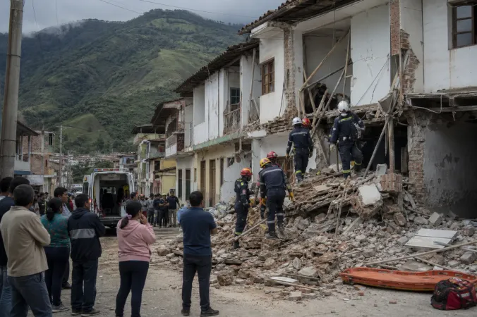 Emergency workers inspect damaged buildings on a street in western Colombia after an earthquake, with mountains in the distance.