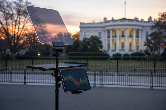 A teleprompter stand outside the White House at dusk with abstract financial market charts on a nearby monitor.
