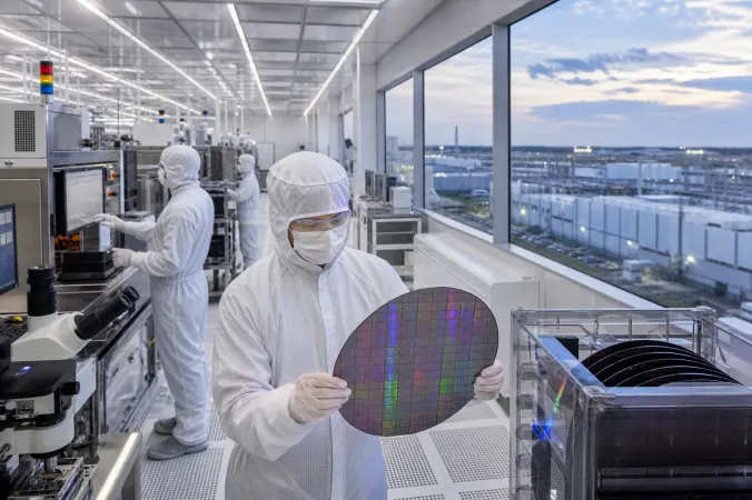 Engineers in cleanroom suits inspecting semiconductor wafers and process equipment inside an advanced fabrication facility.