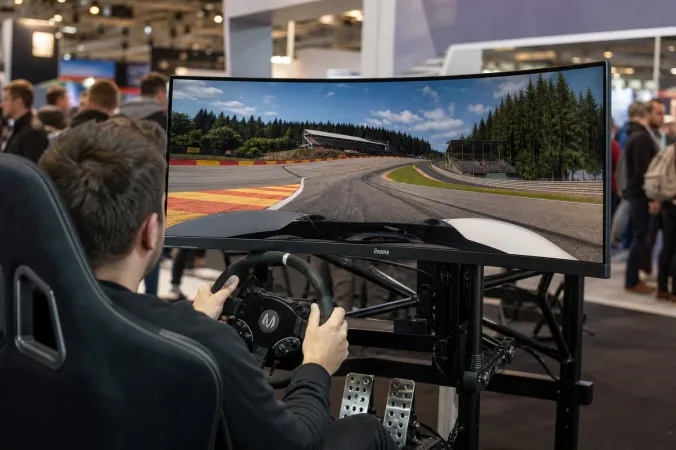 A 49-inch curved iiyama G-Master Gold Phoenix monitor installed in a sim-racing cockpit with steering wheel and pedals at a gaming exhibition.